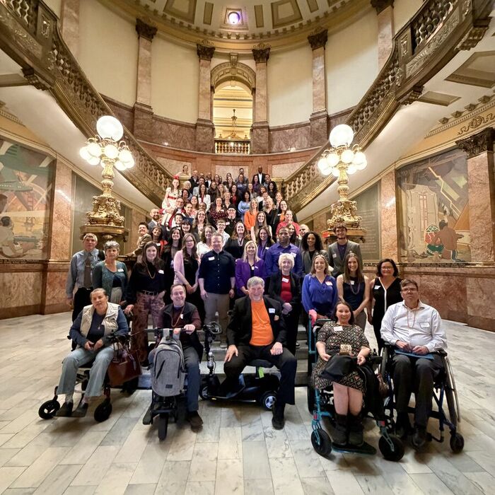 CRDC members and families, several using wheelchairs and mobility scooters, gathered on the marble staircase beneath the Colorado State Capitol rotunda.