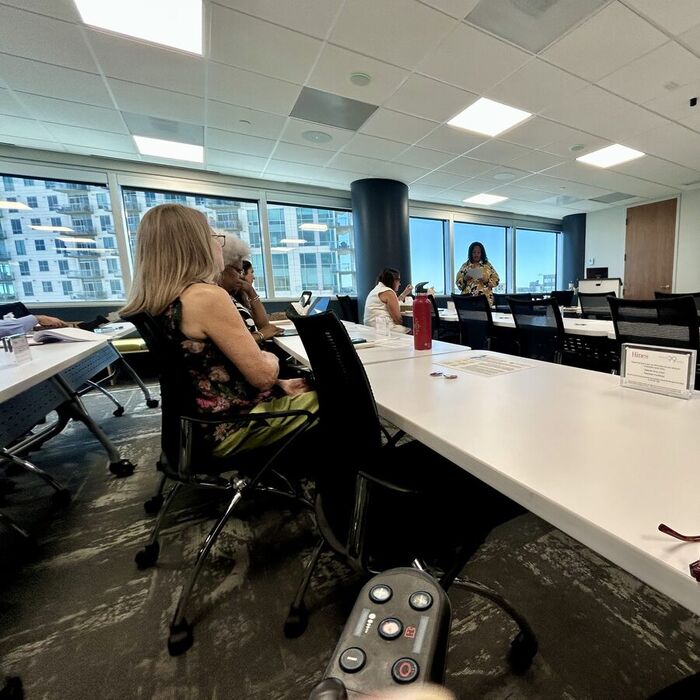 Taskforce members seated around a long conference table while a speaker presents policy slides.