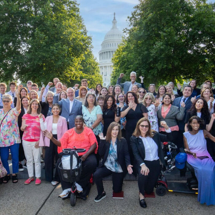 A large group of advocates waving and cheering outside the United States Capitol in Washington, DC, several using wheelchairs and mobility aids.